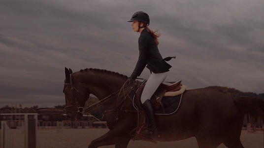 Cavalière en tenue d’équitation montant un cheval brun en action sur une piste d’entraînement.